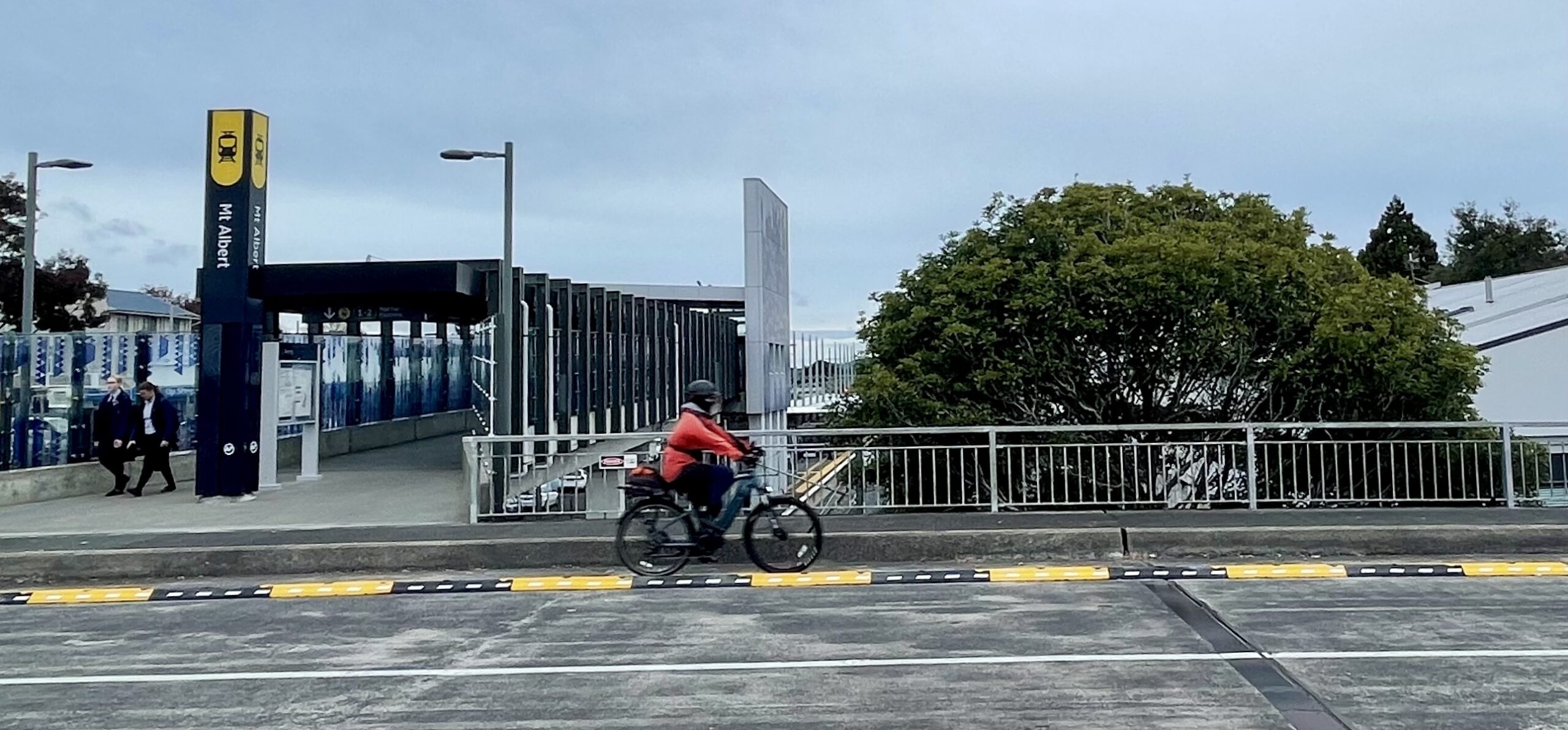 A person riding a bike in a protected cycleway past the entrance to the Mt Albert railway station