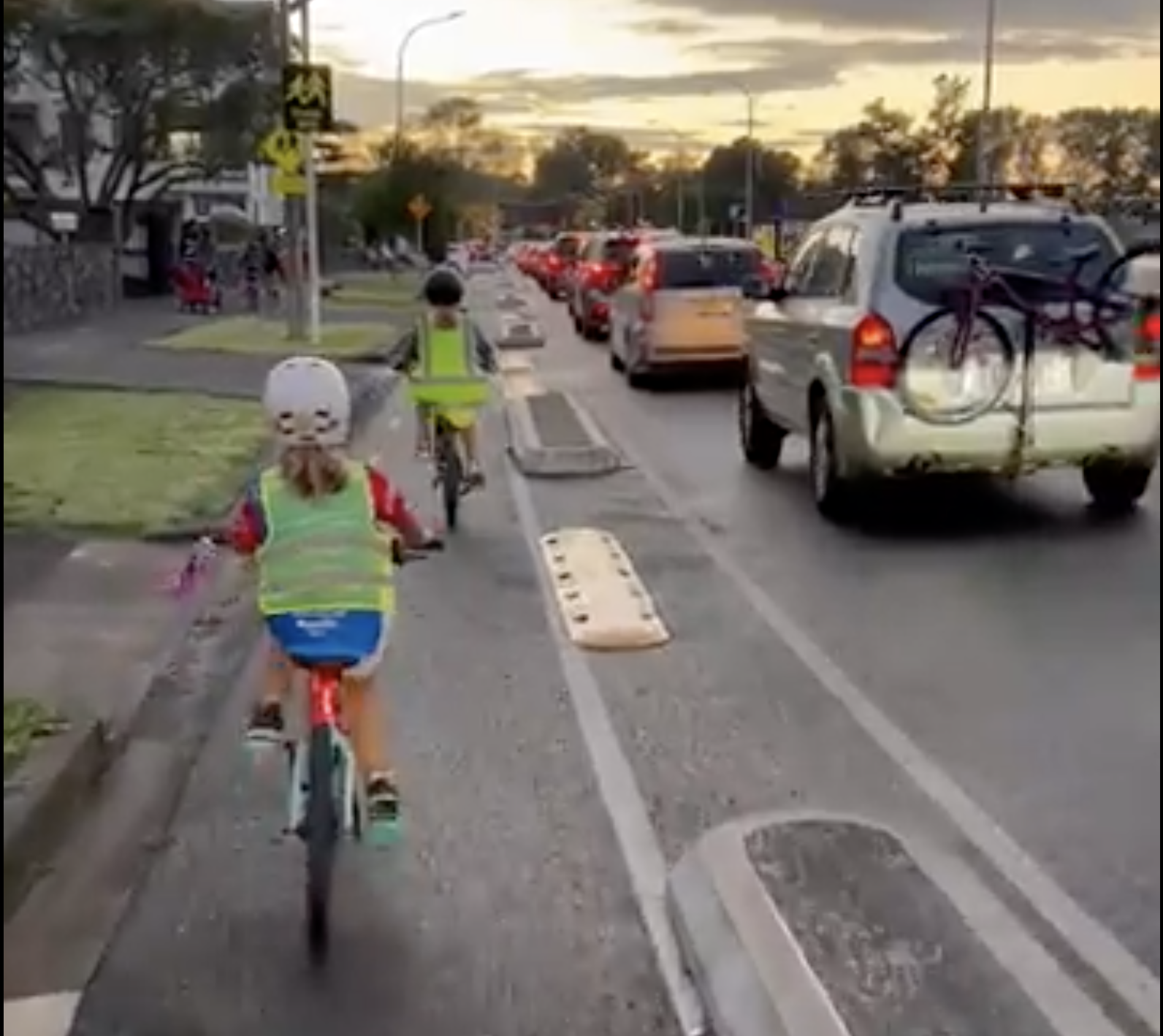 Children riding in the protected cycleway along Taniwha st. There is a row of car traffic beside the safe cycleway. 