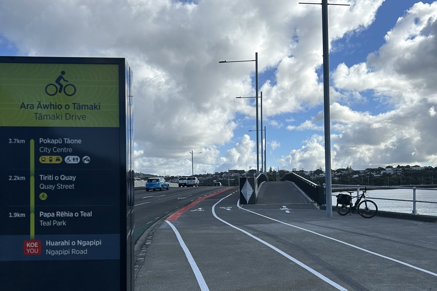 A bridge with sparated sections for pedestrians, bikes, and cars. A bike is leaning against the railing over looking the sea.