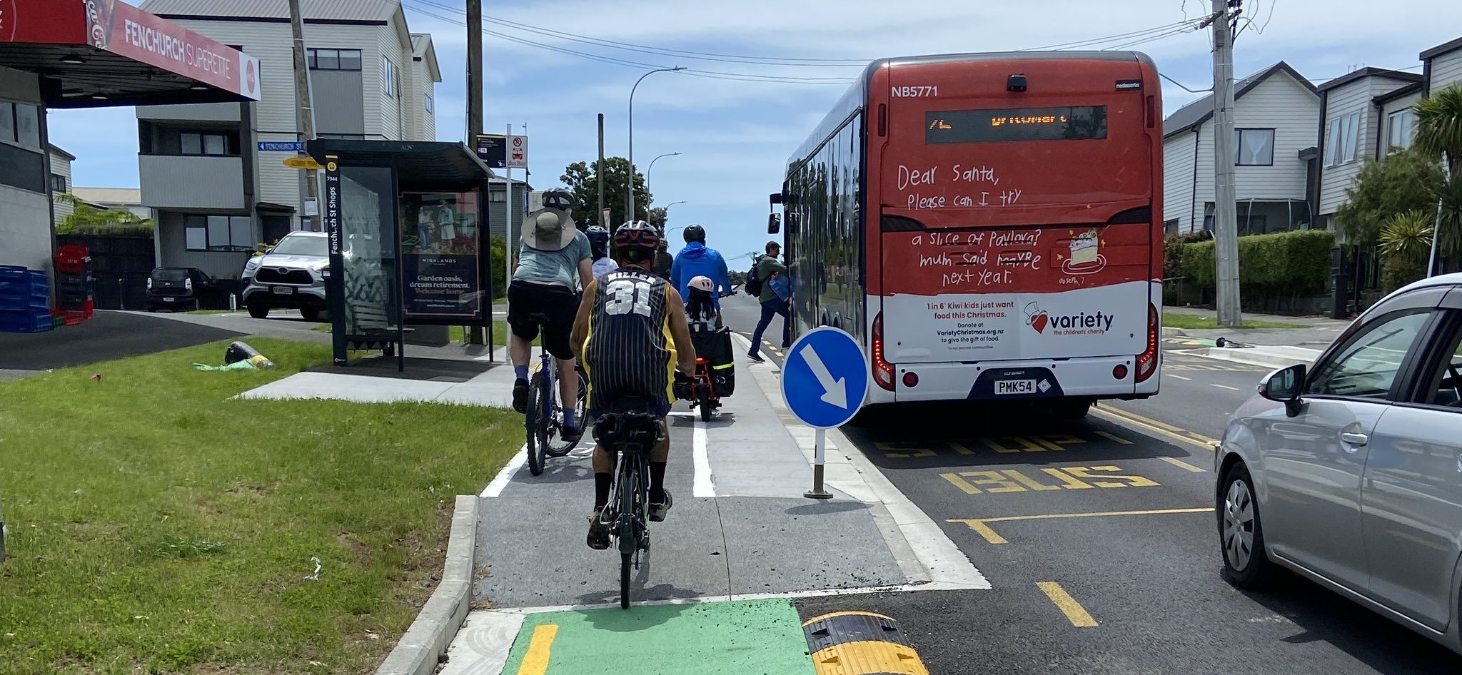 Several people riding bikes cross the raised platform bus stop, while bus passengers get onto a waiting bus 