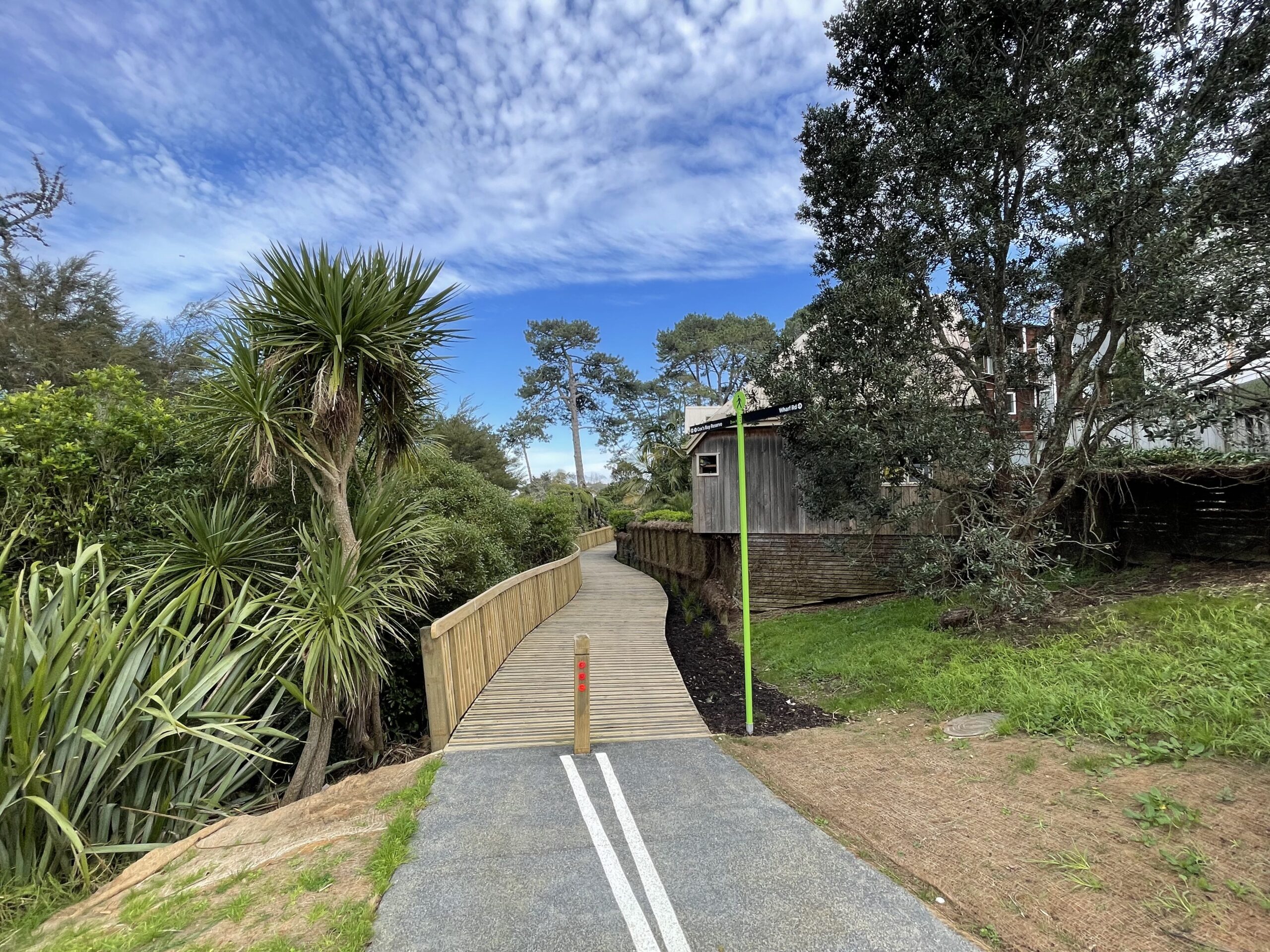 A path leads onto a wooden bridge, with bush on one side and a house on the other