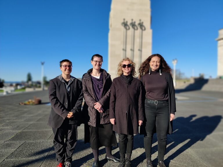 Four people in black stand before the cenotaph on a sunny winter afternoon