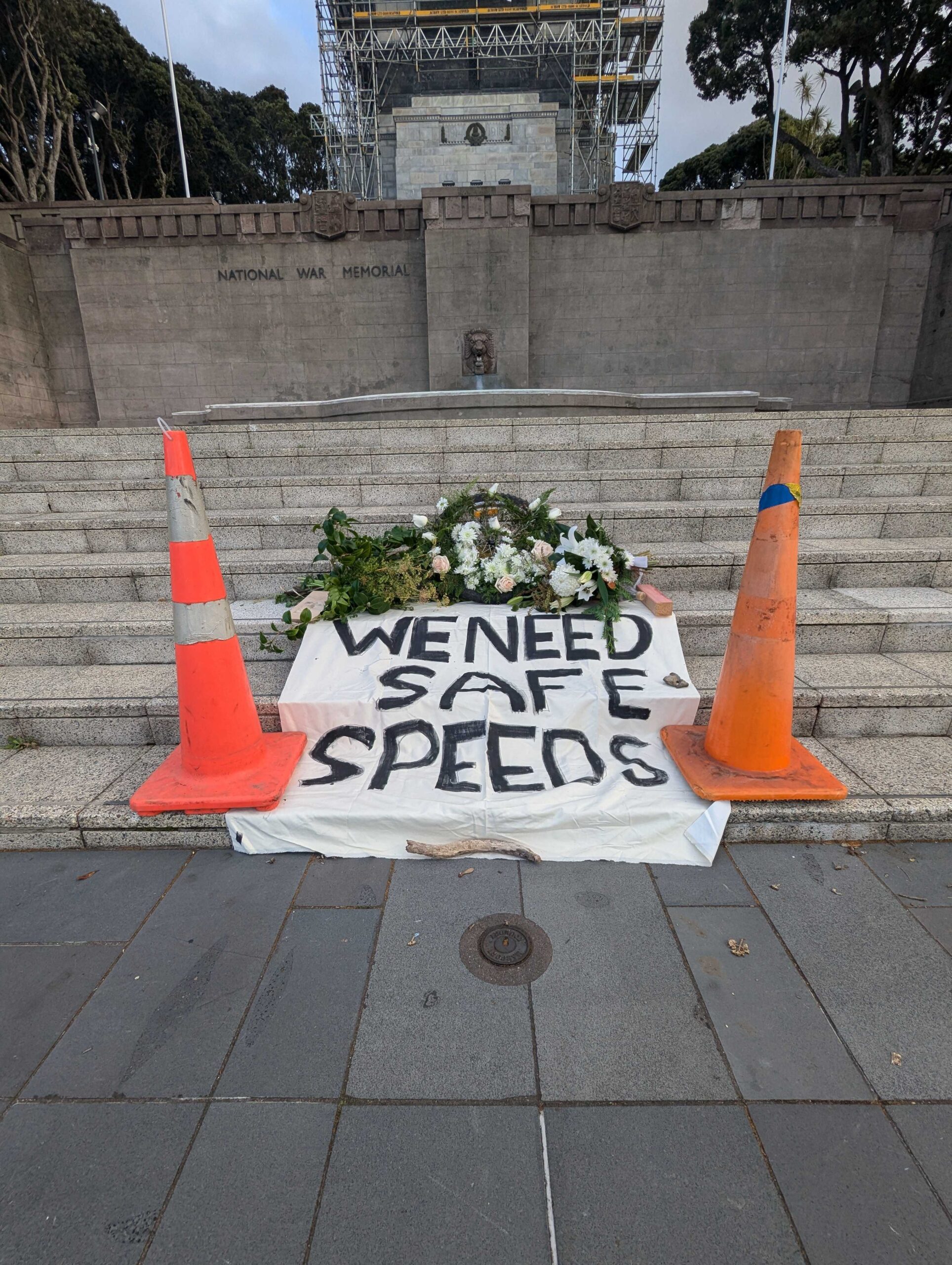 A wreath on steps with road cones and a sign "we need safe speeds"