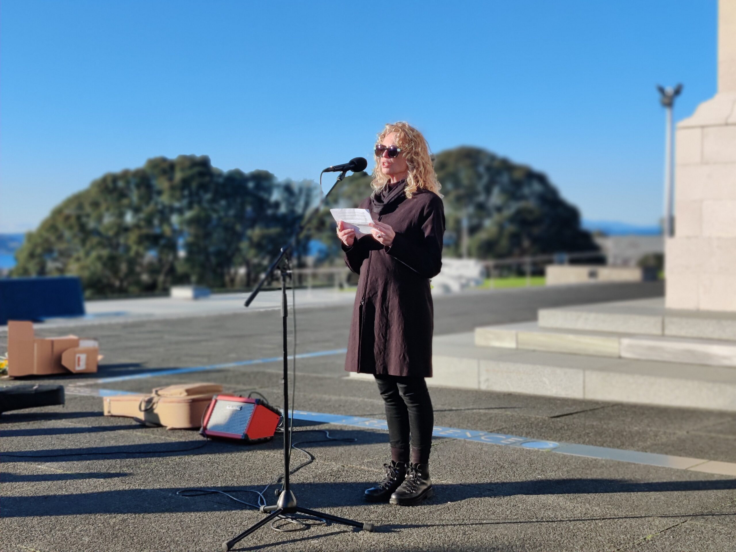A woman speaks into a microphone in front of a cenotaph