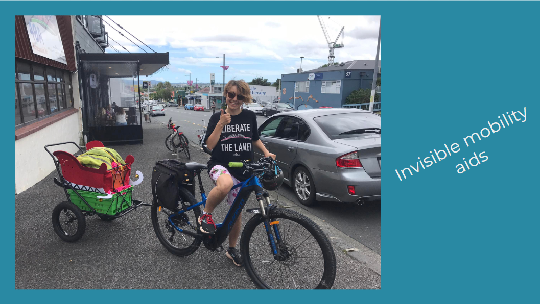 Fiain sits on a bike and grins, thumbs up. There is a bike trailer attached to their bike which has been decorated to look like Santa's sleigh. Next to the photo are the words "invisible mobility aids"