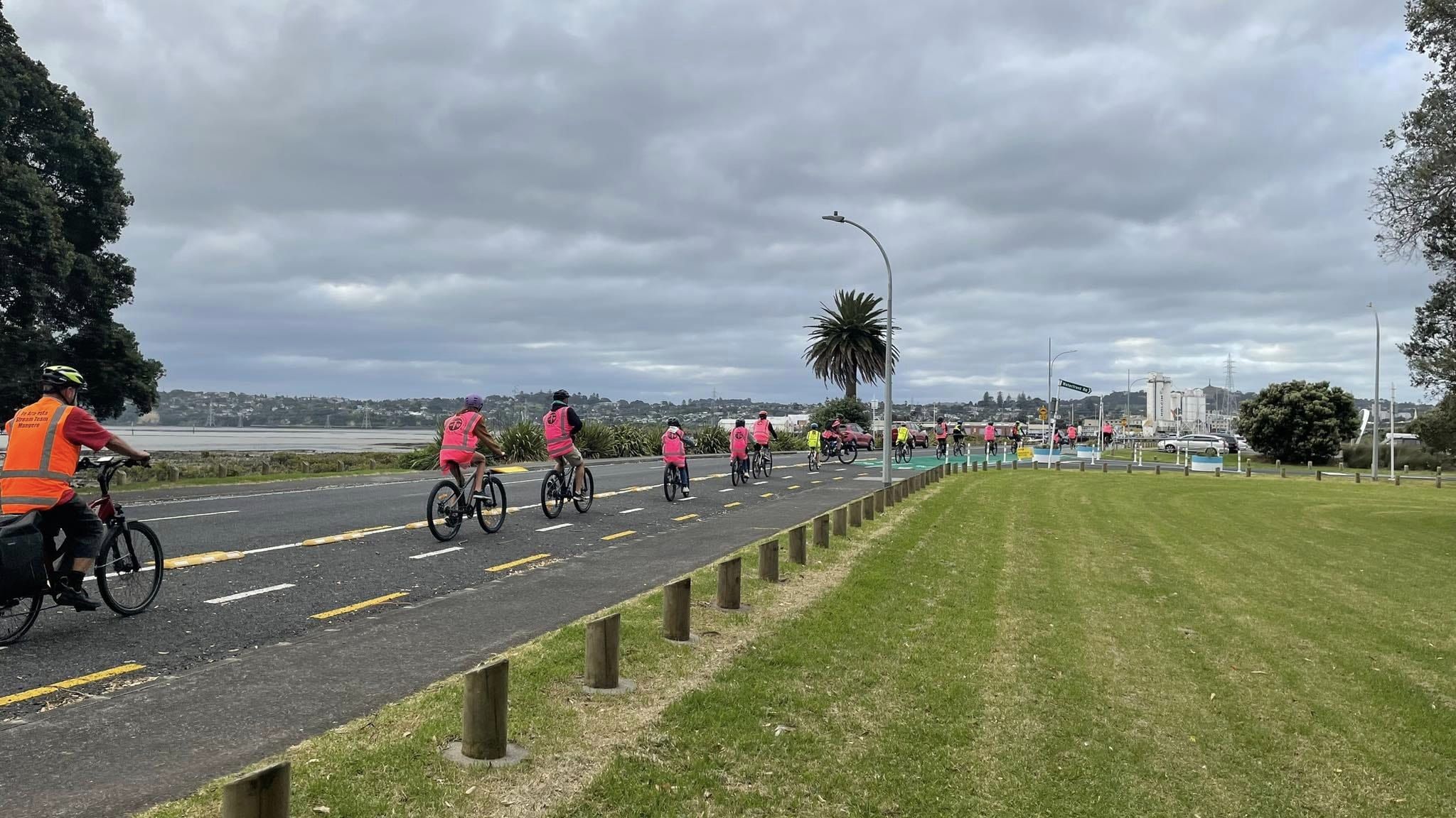 Photo: An on-road bi-directional cycle lane with minimal protection. On it, multiple high-vis vested people on bikes are travelliing Northbound. 