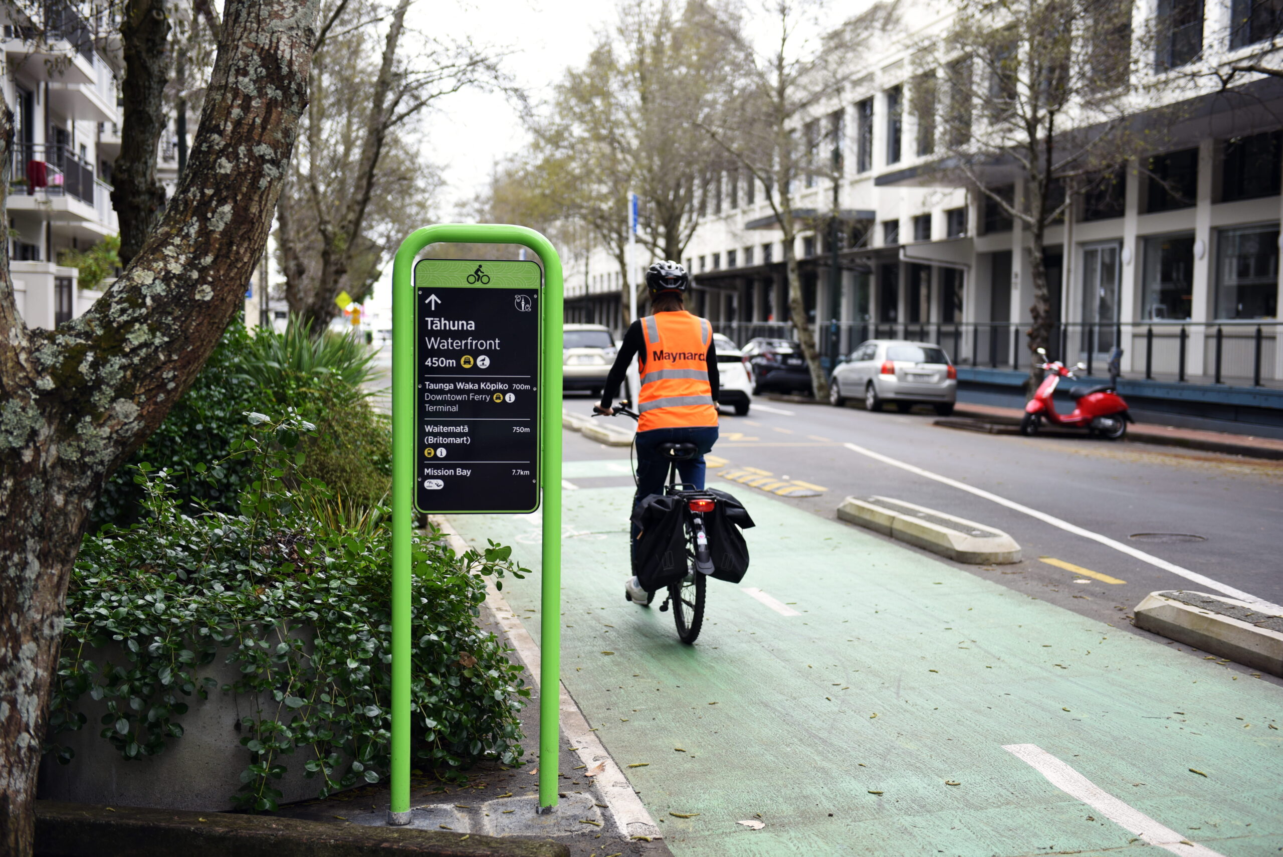 Person on bike rides up cycleway on urban street past a wayfinding sign