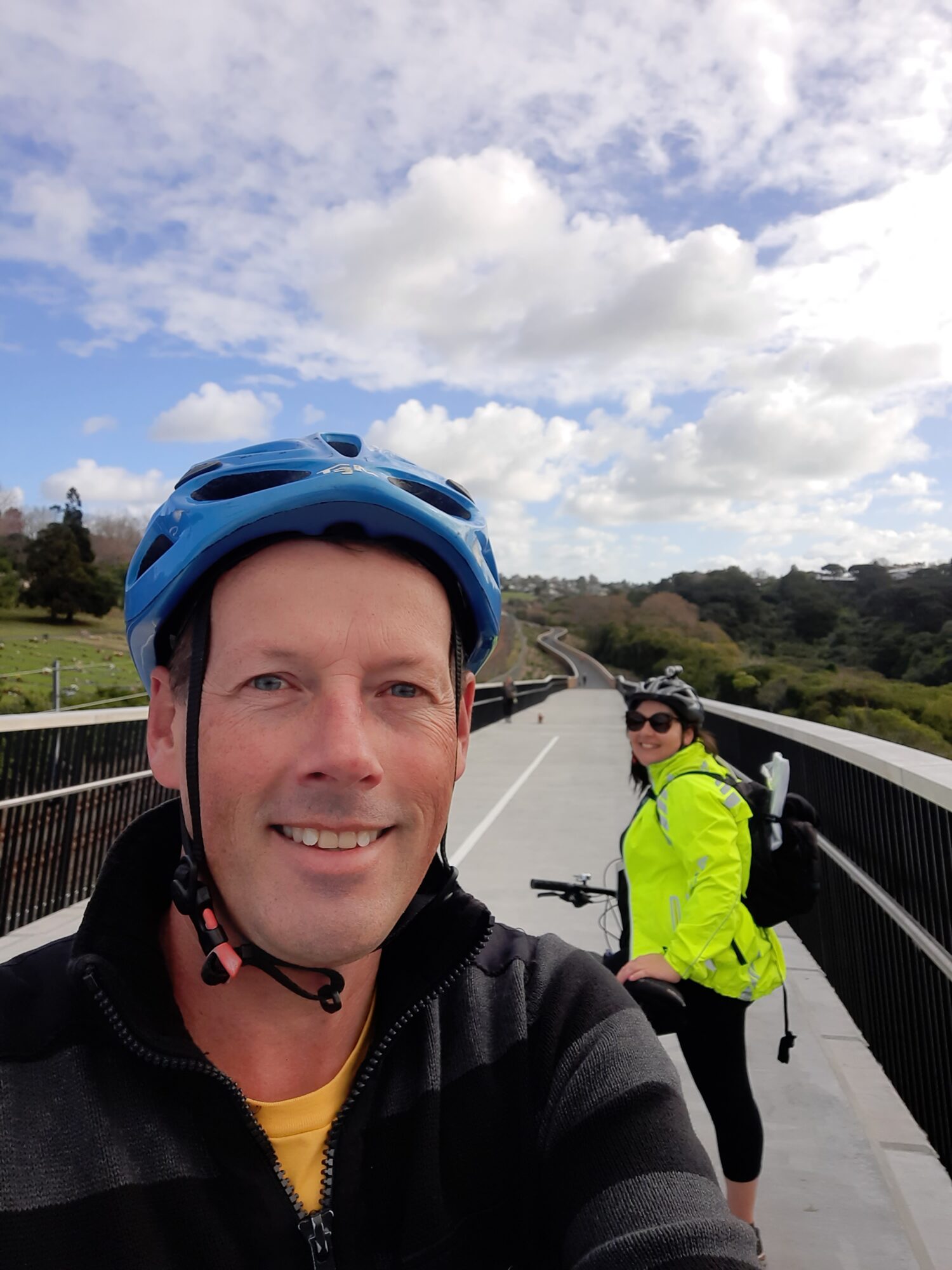 Selfie style image of Mark smiling and another person on a bike on a cycleway