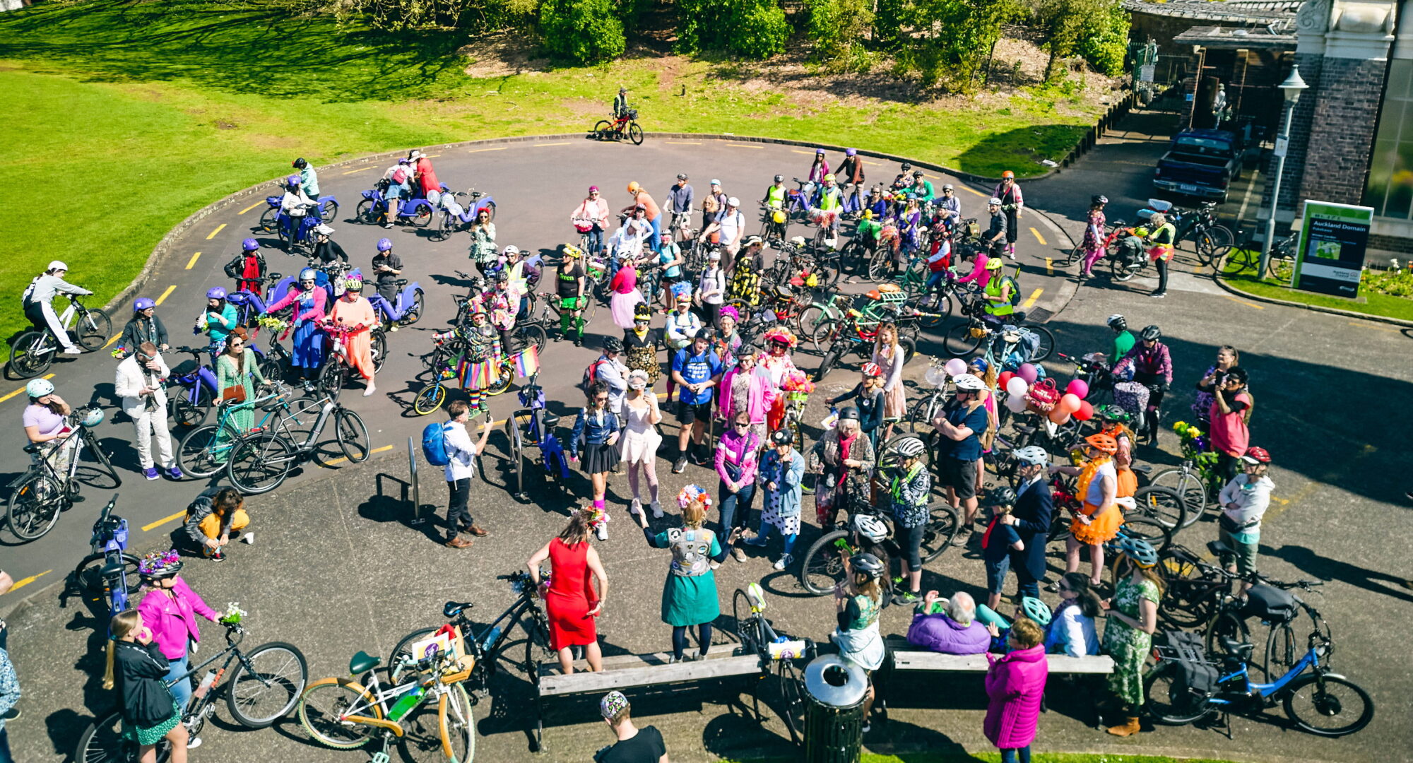 Large group of colourful folks with bikes in a park, seen from above