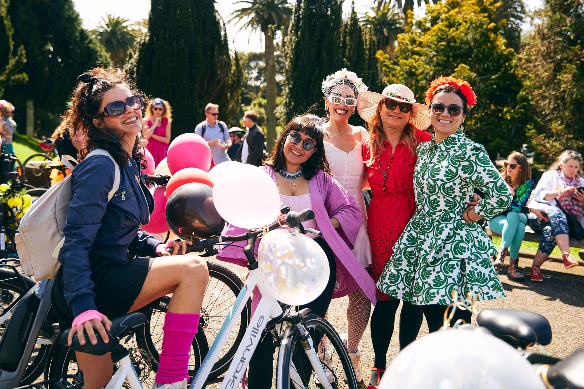 Women in colourful clothes pose with a bike that has balloons on it