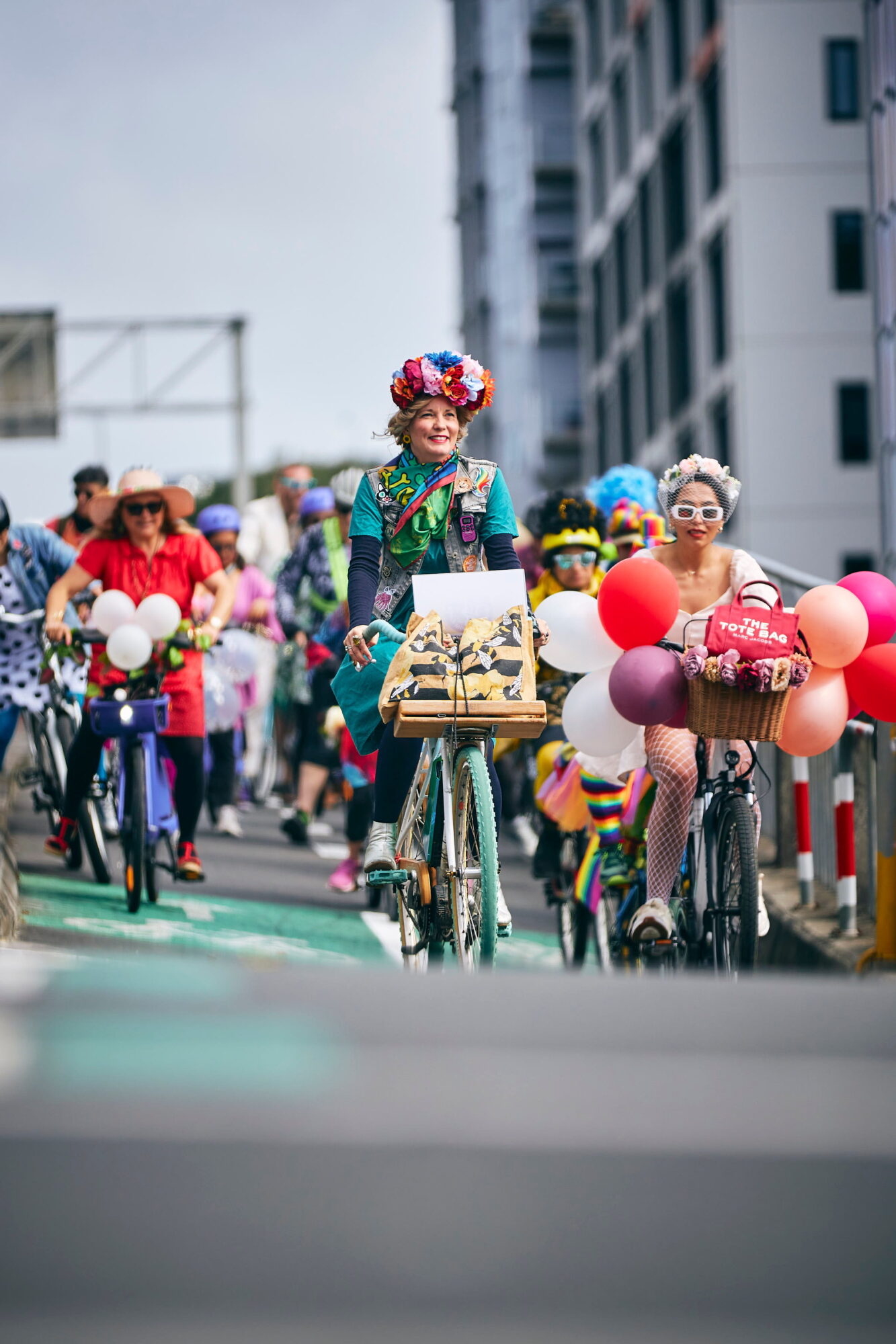 a colourful woman with flowers in her hair leads a large group of people on bikes down a hill