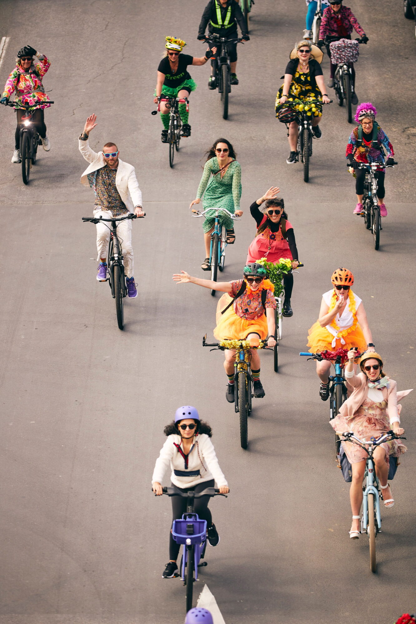 12 or so colourful people cycling along a road, seen from above