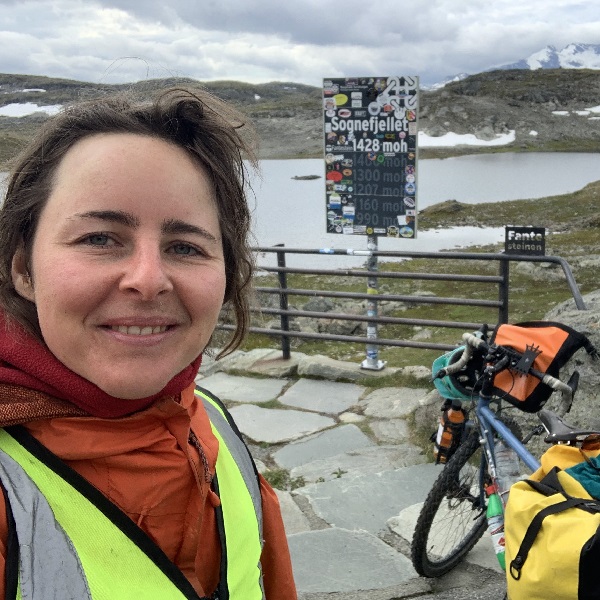 Phoebe is smiling, her bike is in the background with bikepacking gear strapped to it.