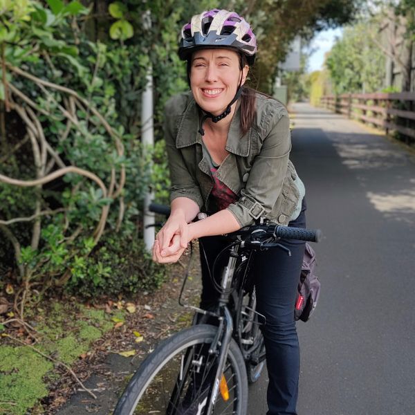 Sue is a white pakeha woman on a leafy cycleway, smilng