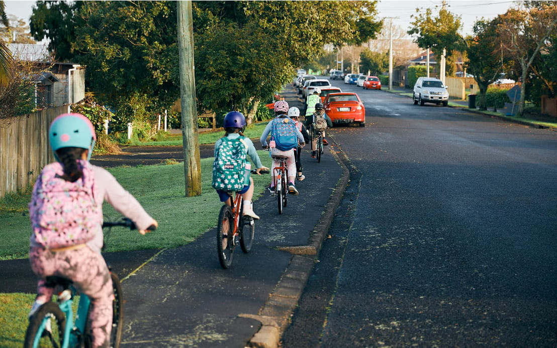 A line of 6 or so kids on bikes head up a suburban footpath