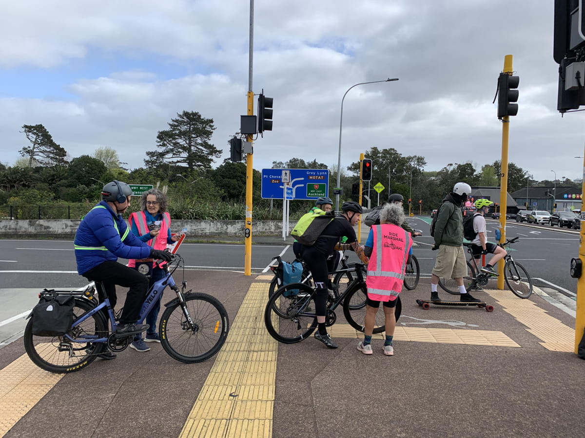 Two volunteers in high vis talking to cyclists at an intersection