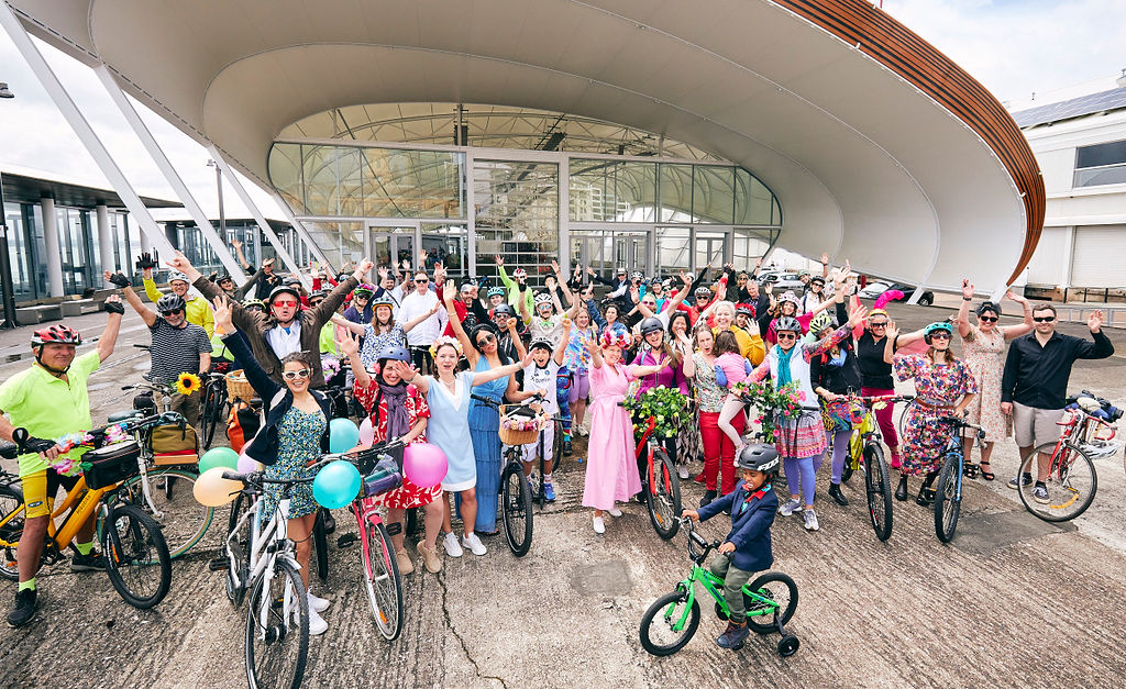 A big colourful group of people and bikes in front of the Cloud