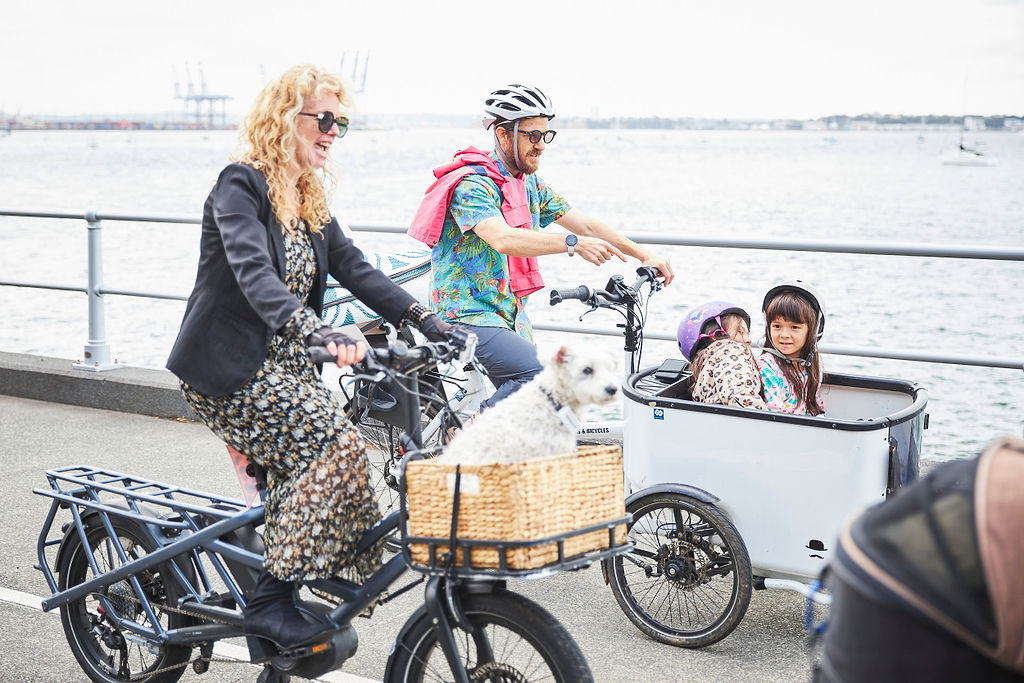 One bike has a small dog in the front basket. The other bike has two kids in a cargo bucket on the front.