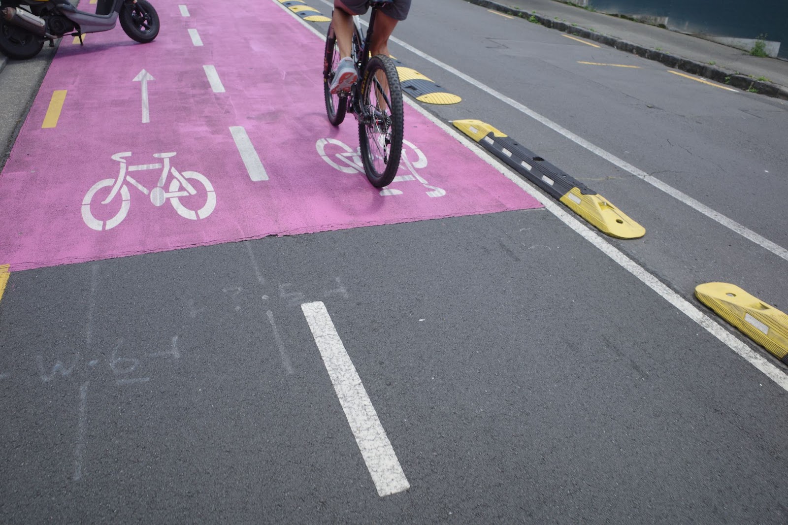 Two way cycleway with rubber protection alongside. A cyclist rides around a moped parked partly in the cycleway