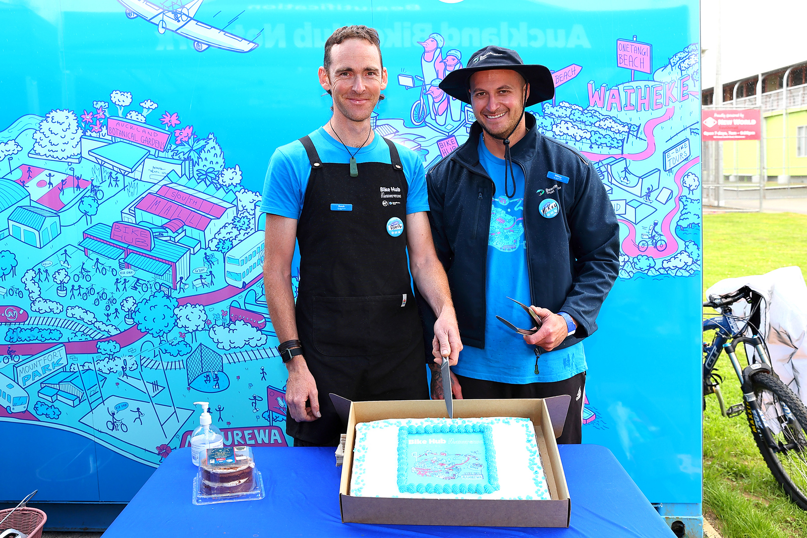 Reesh and Mikey stand ready to cut a large blue cake