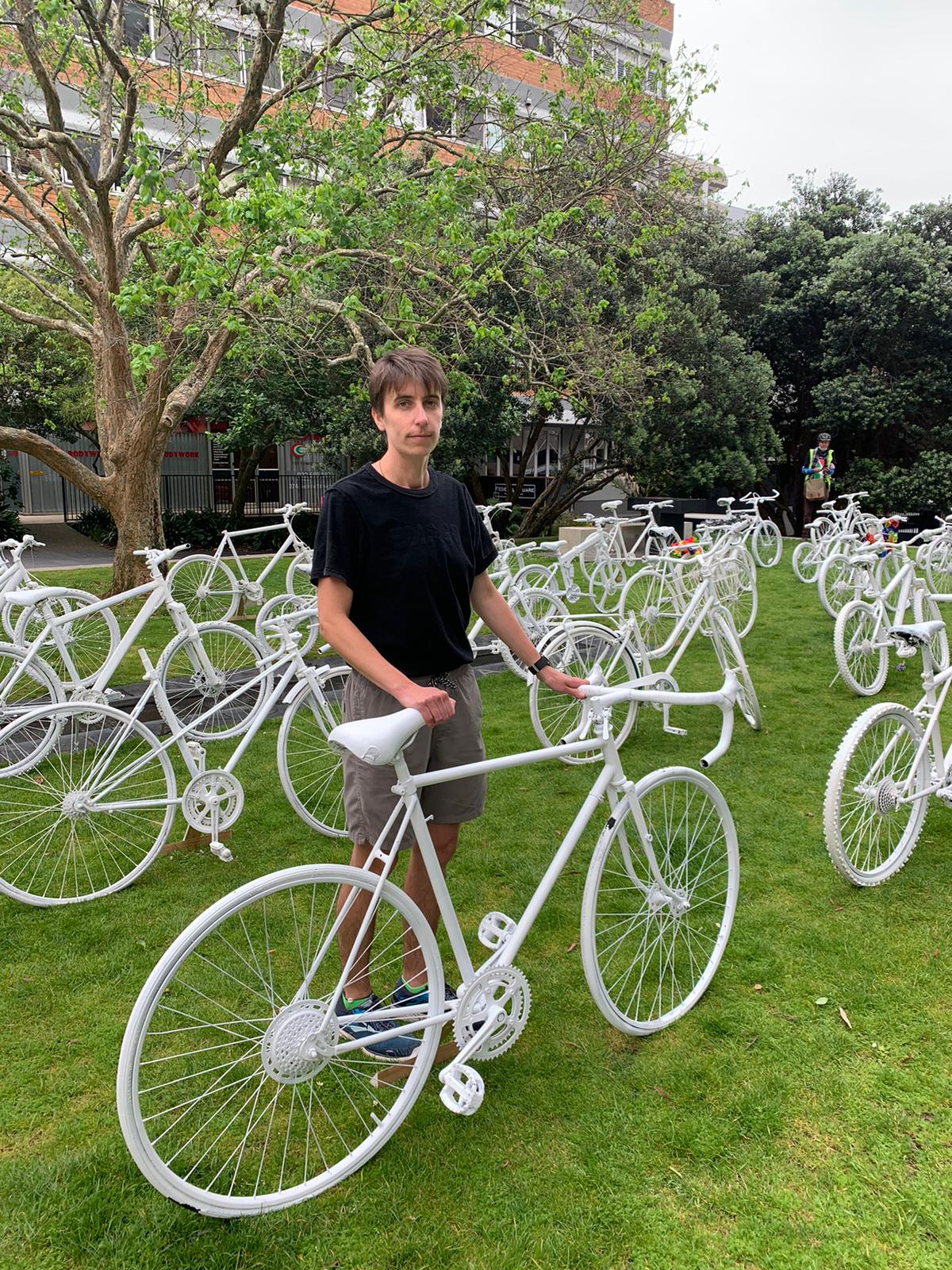 Lucy holds a ghost bike, many more stand on the grass behind her