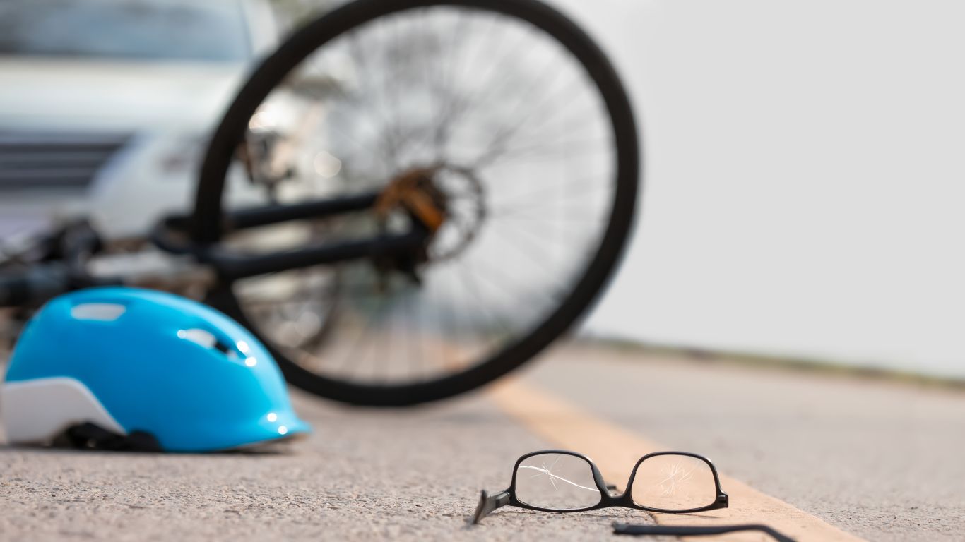 scene of a bike crash with a helmet and broken glasses on the road, and a car in the background