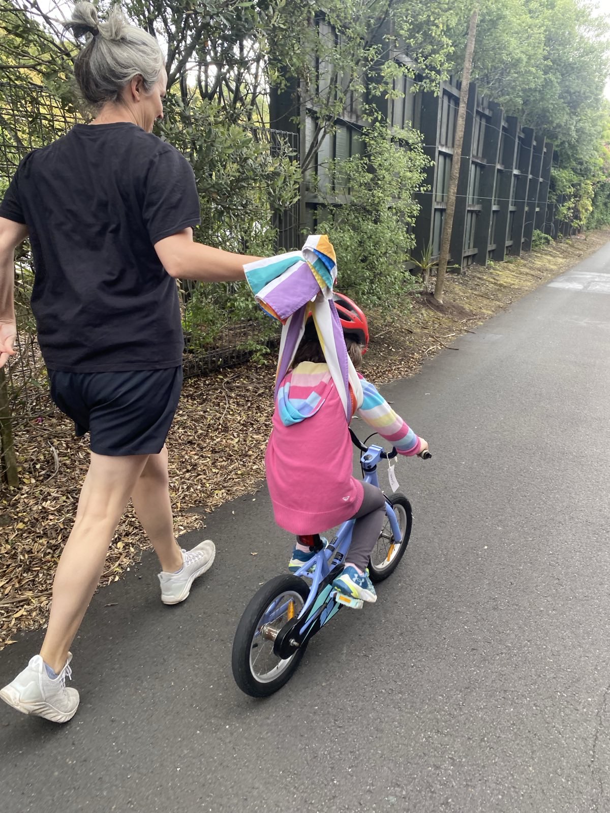 Mum holds kid learning to ride a bike with the towel technique